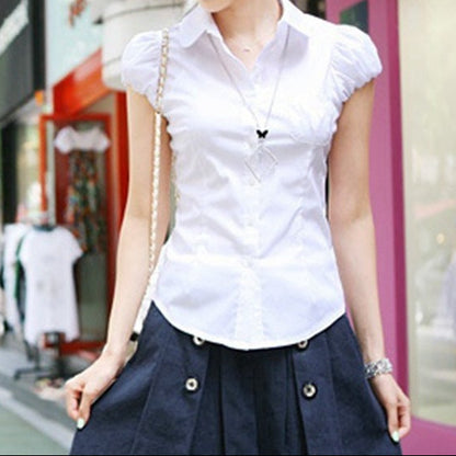 Woman wearing a white blouse with short sleeves and a navy skirt on a city street.
